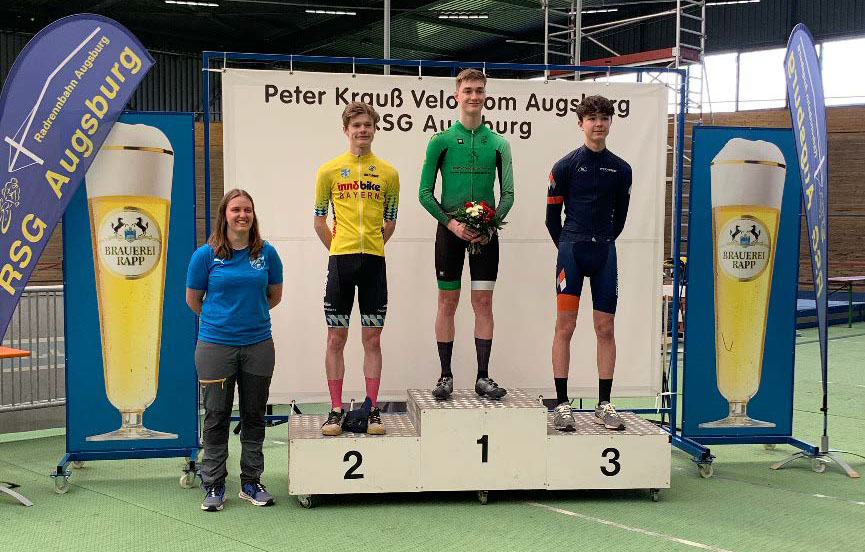 Nico Wollenberg von den KTM Youngsters auf dem zweiten Platz auf einer Tribüne. Er trägt ein gelbes Trikot und Bibshorts von DOWE Sportswear.