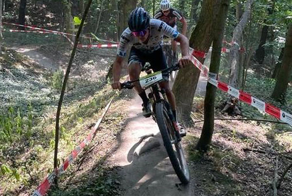 Zwei Mountainbiker fahren . Ausgestattet mit Startnummern brausen sie durch eine holprige Strecke im Wald, begrenzt von Absperrbändern.