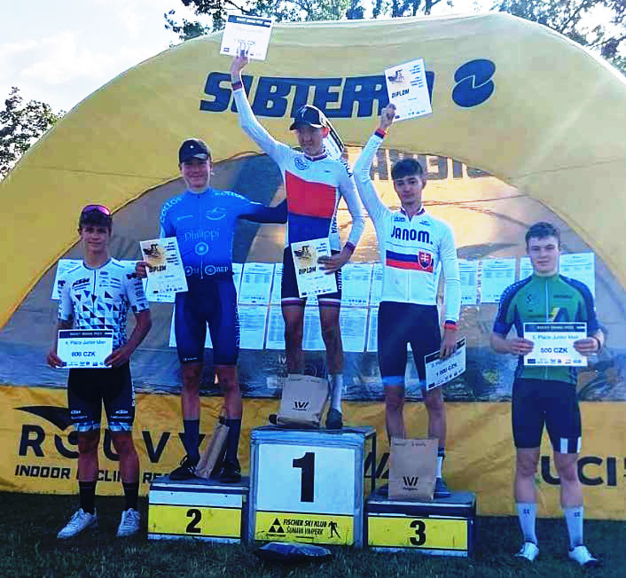 Fünf Radsport-Athleten auf / um eine Tribüne. Sie tragen verschiedene Trikots und halten alle Urkunden.